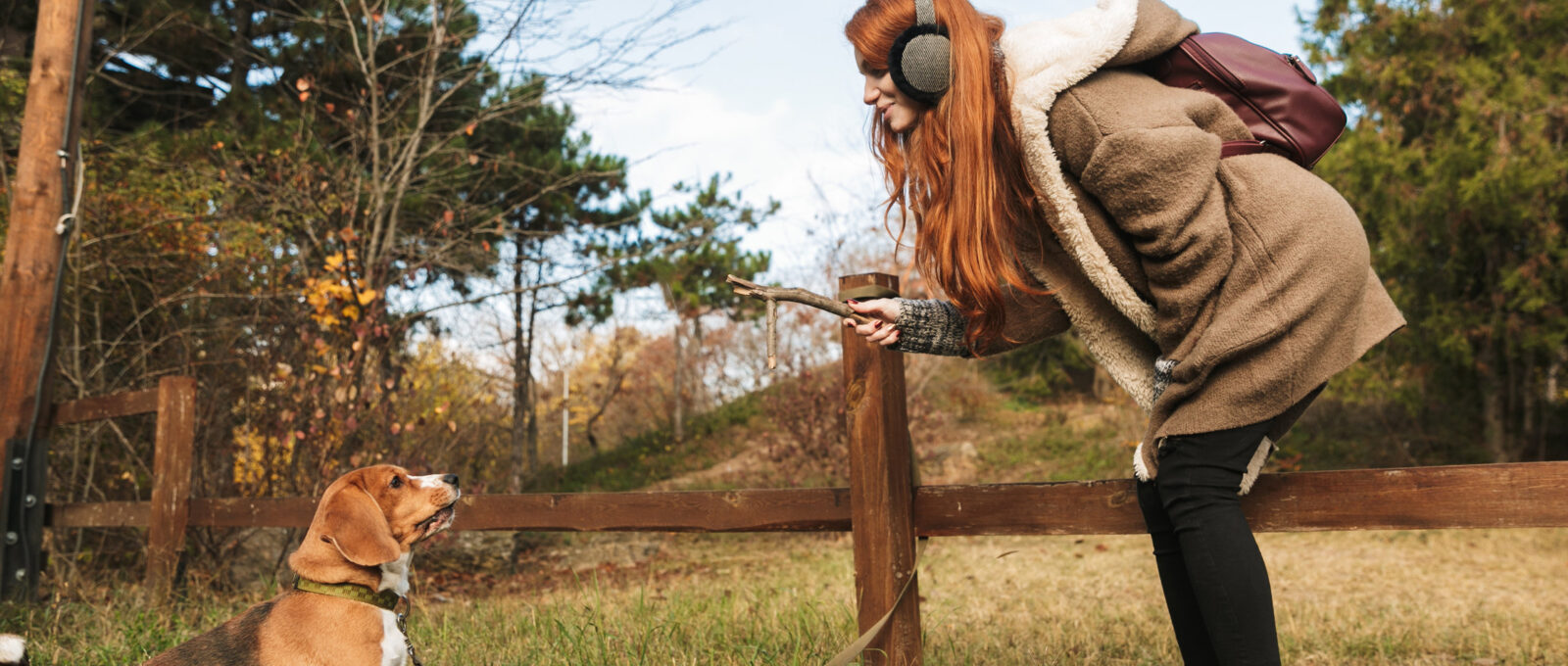 Redhaired girl with headphones crouches towards Beagle dog.